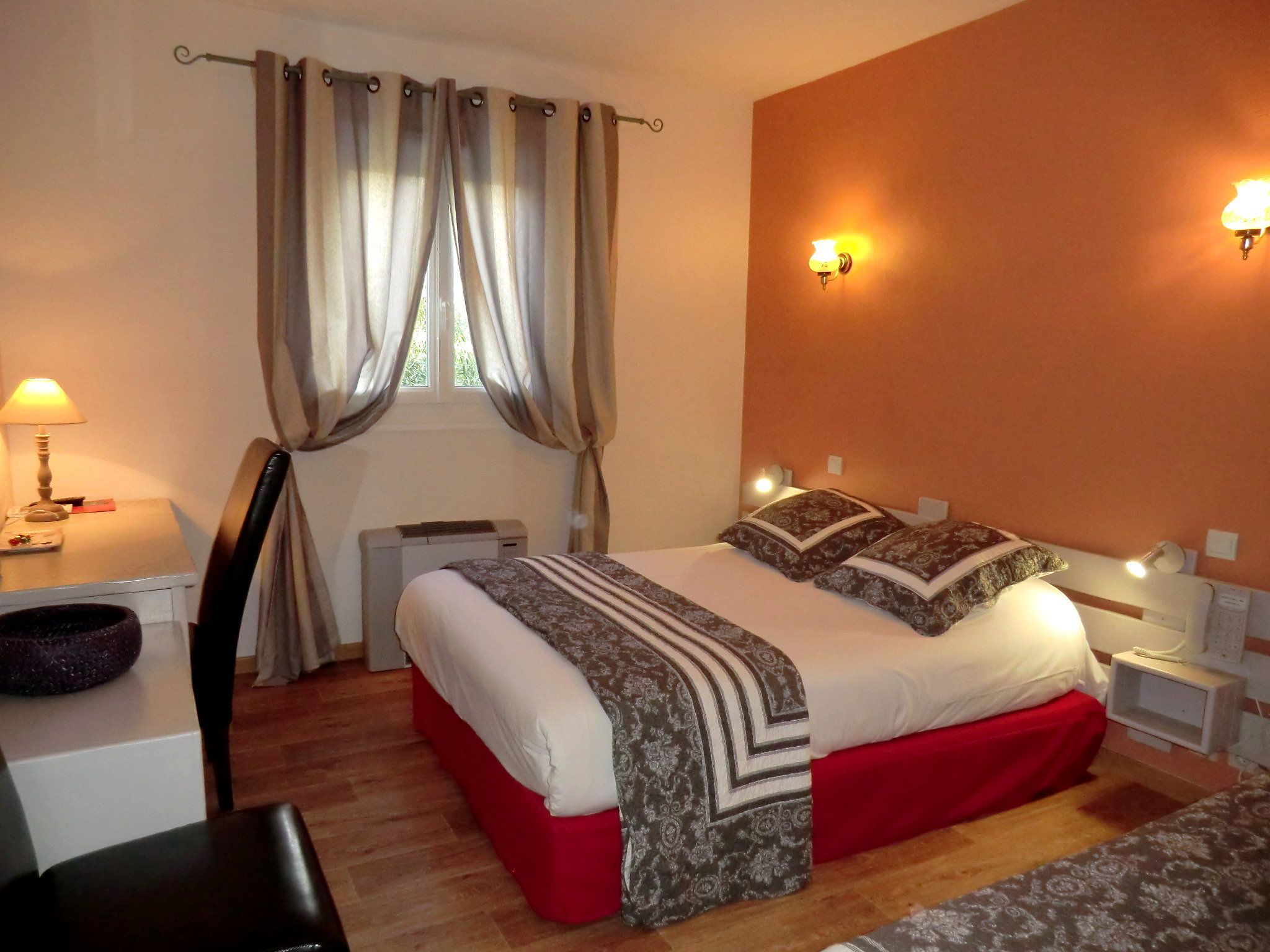 A bedroom with a bed, a desk, a chair, a heater, and two wall-mounted lights.