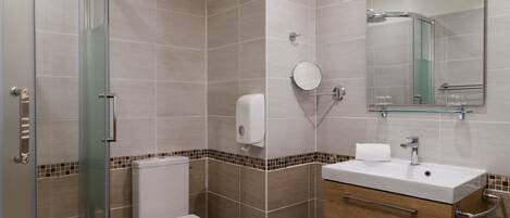 A modern bathroom with a glass shower enclosure, a toilet, a sink with a mirror, and a towel dispenser.