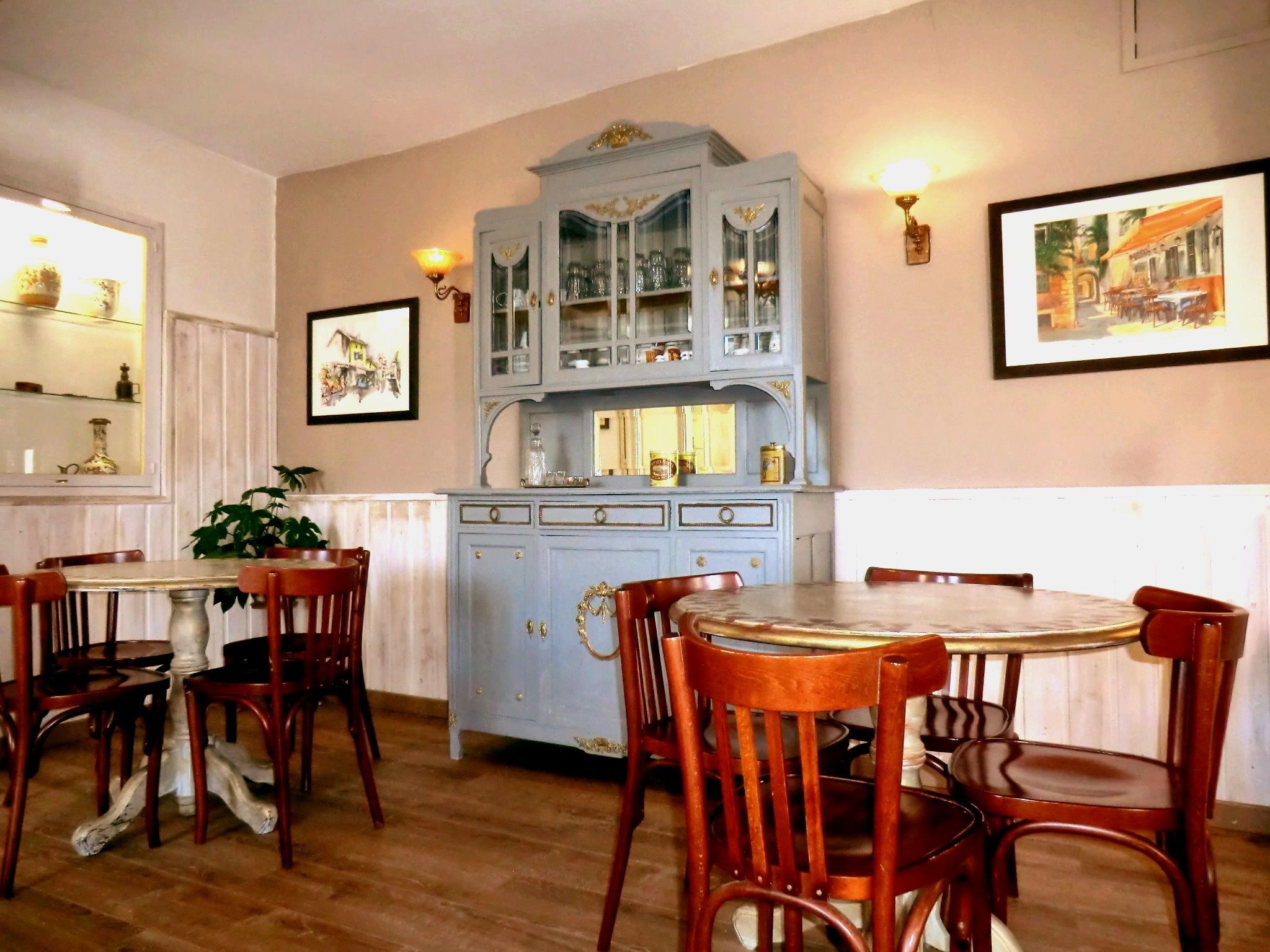Un coin repas avec des chaises en bois et une table, un meuble bleu clair avec des portes en verre, et un tableau encadré au mur.