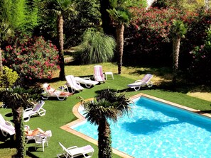 A pool area with multiple lounge chairs and a swimming pool surrounded by greenery and flowering plants. - The Originals City, Hôtel du Parc, Avignon Est (Entraigues-sur-la-Sorgue)