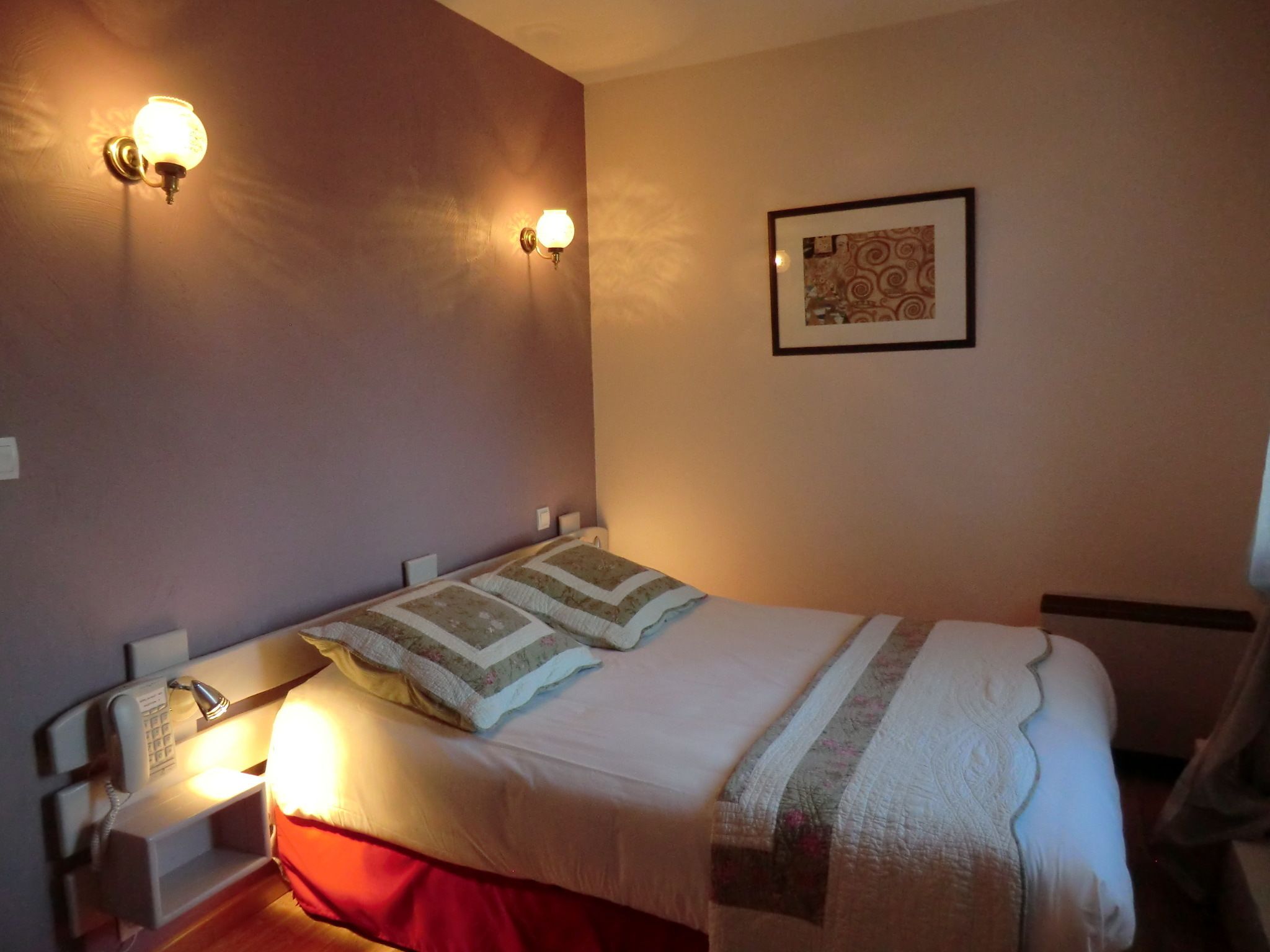Habitación de hotel con una cama, dos lámparas de pared, un teléfono y un cuadro en la pared.
