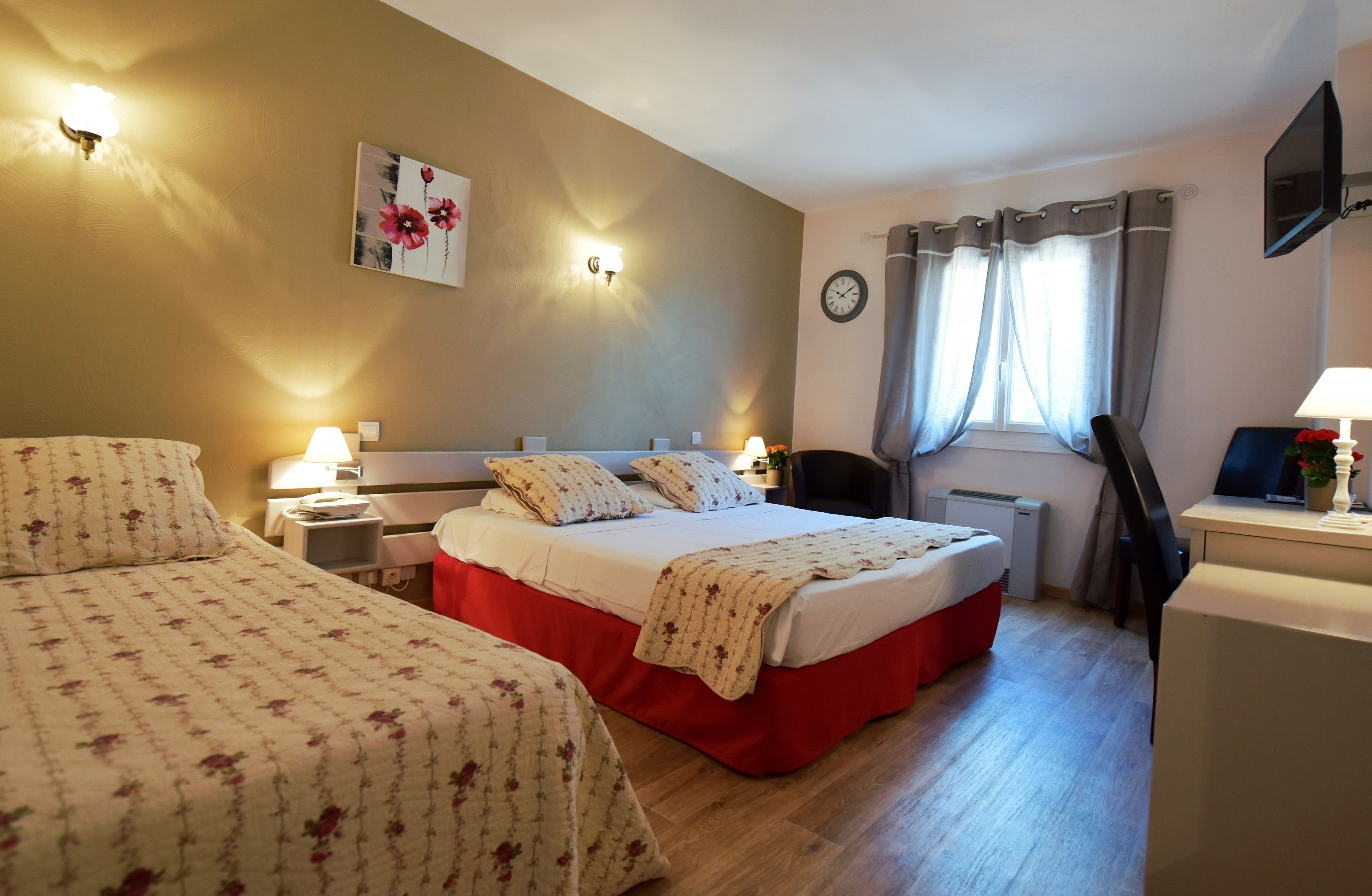 A hotel room with two beds, a desk, a chair, a TV, and a clock on the wall.