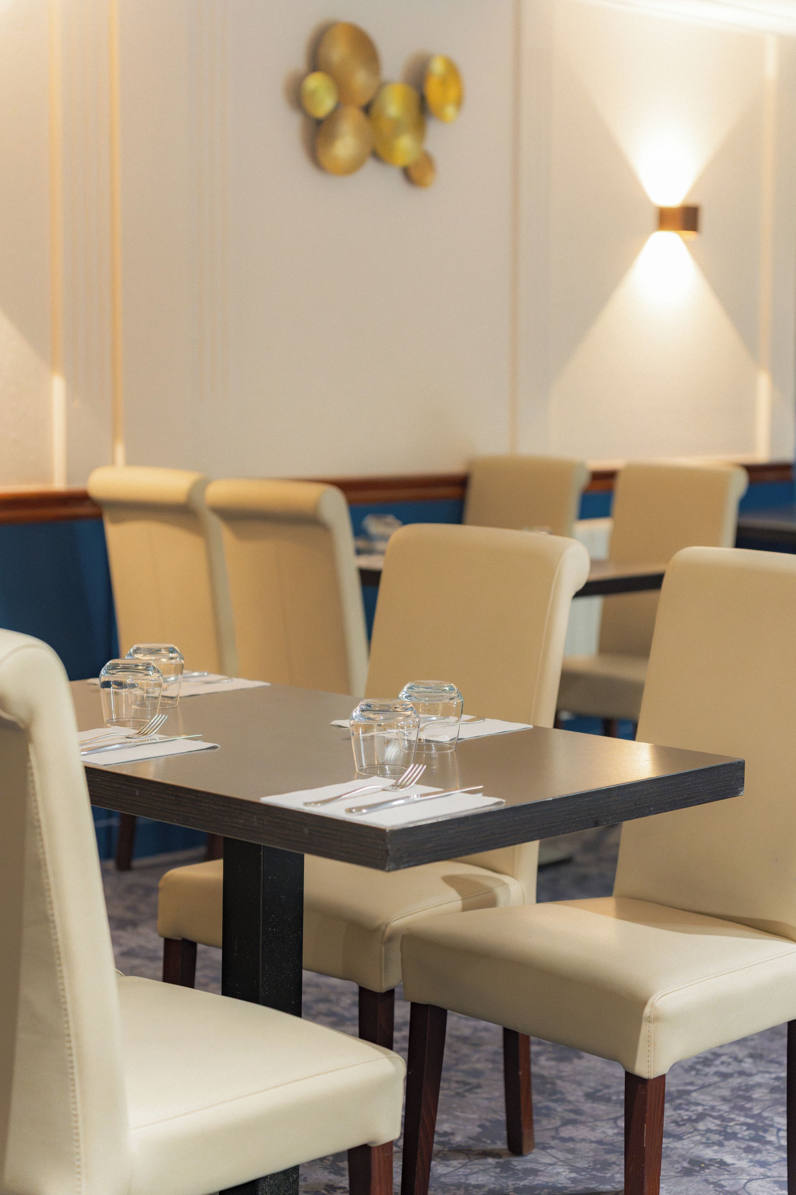 A hotel dining area with tables set for four, chairs, and a wall-mounted light fixture.
