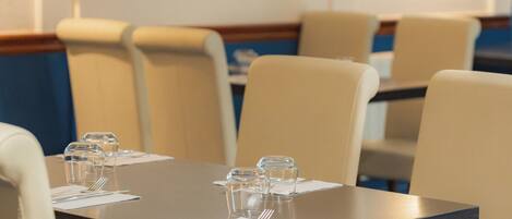 A hotel dining area with tables set for four, chairs, and a wall-mounted light fixture.