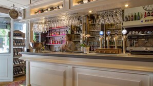 A bar area with shelves of liquor bottles, a clock, and a bar counter with a cash register. - Brit Hotel Chinon le Lion d'Or  (Chinon)