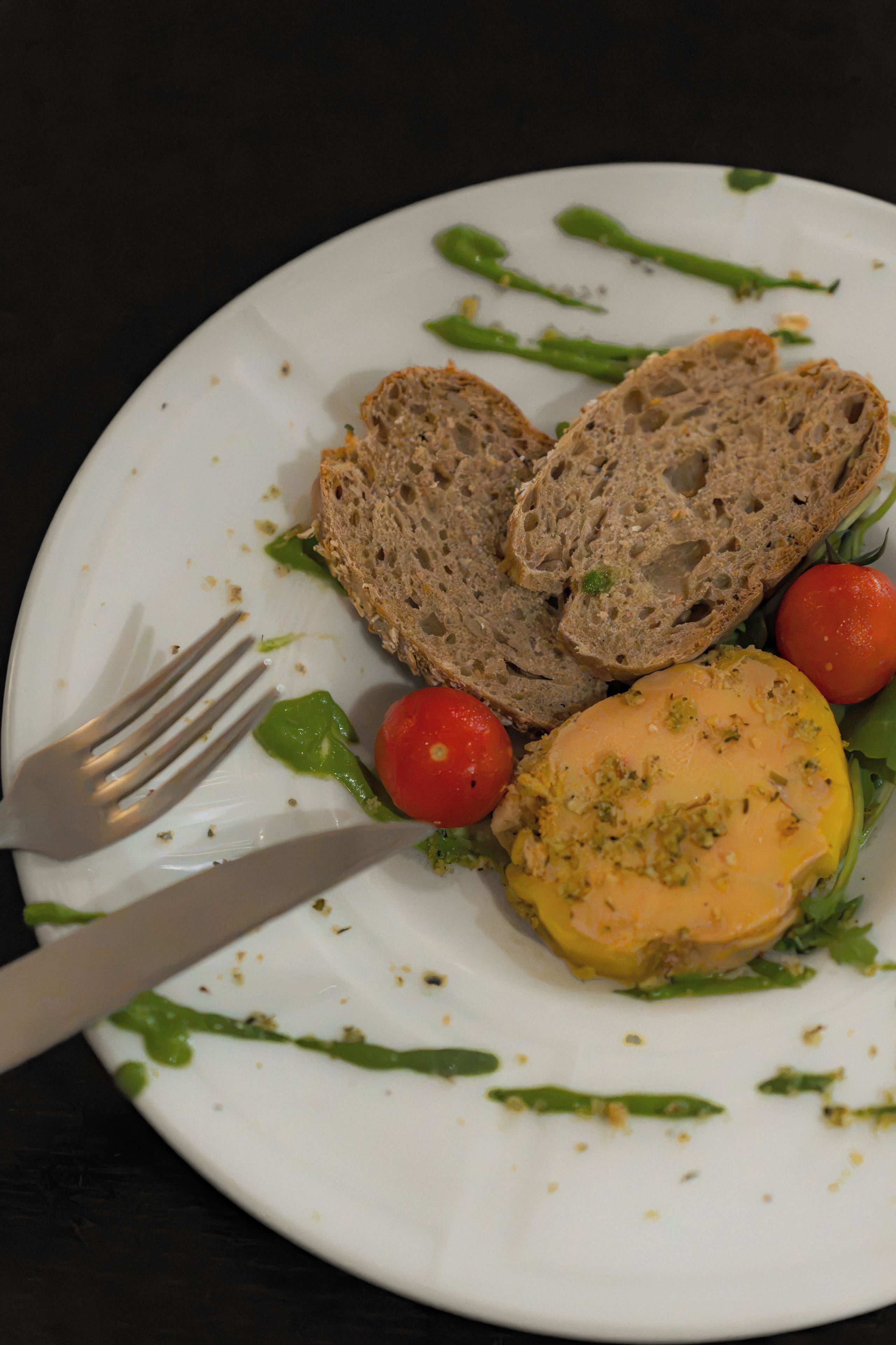 A plate with slices of bread, a tomato, and a yellow spread, possibly a type of cheese or dip.