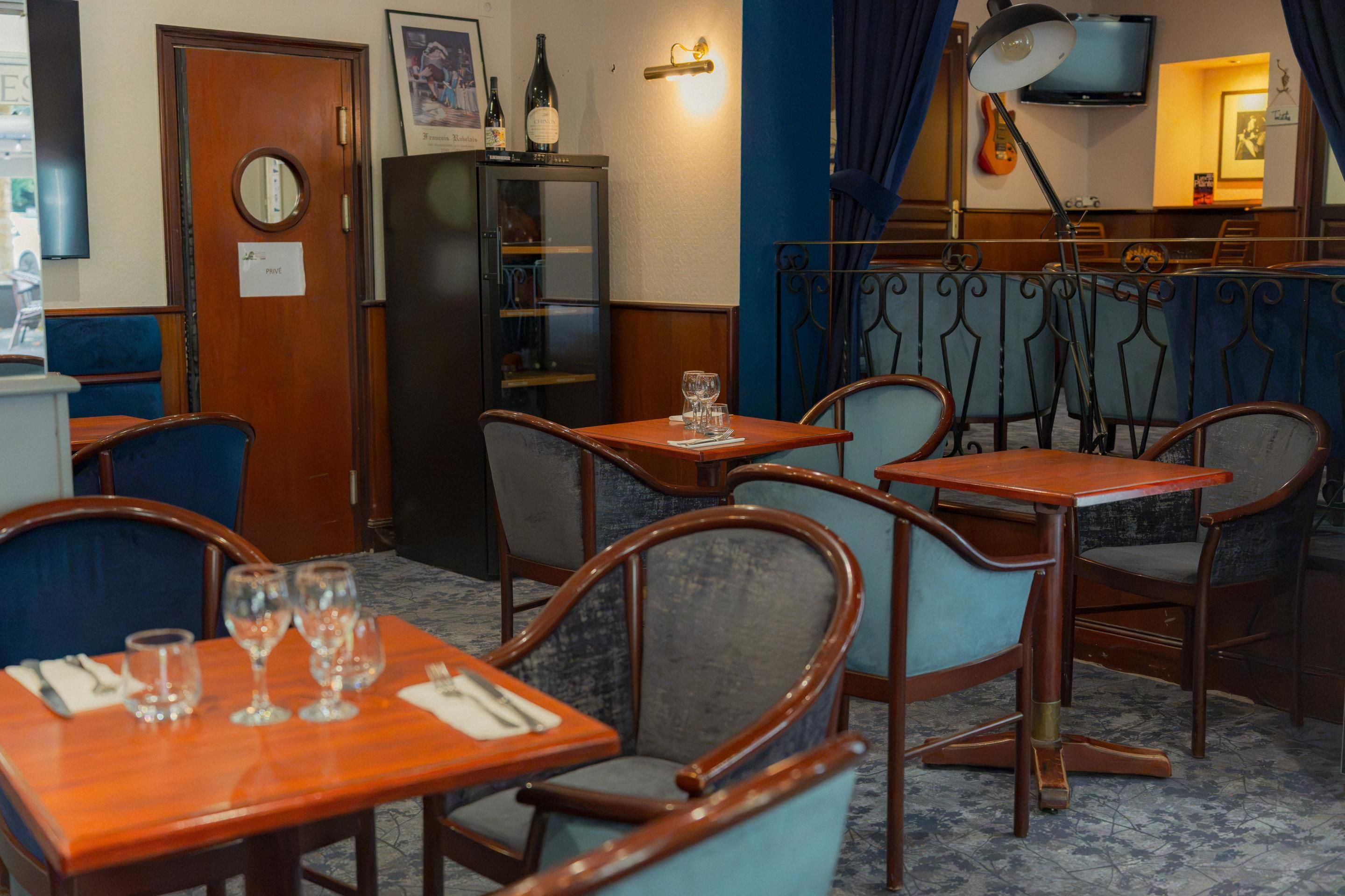 Een restaurantinterieur met houten tafels en stoelen, een klok en een wijnfles aan de muur.
