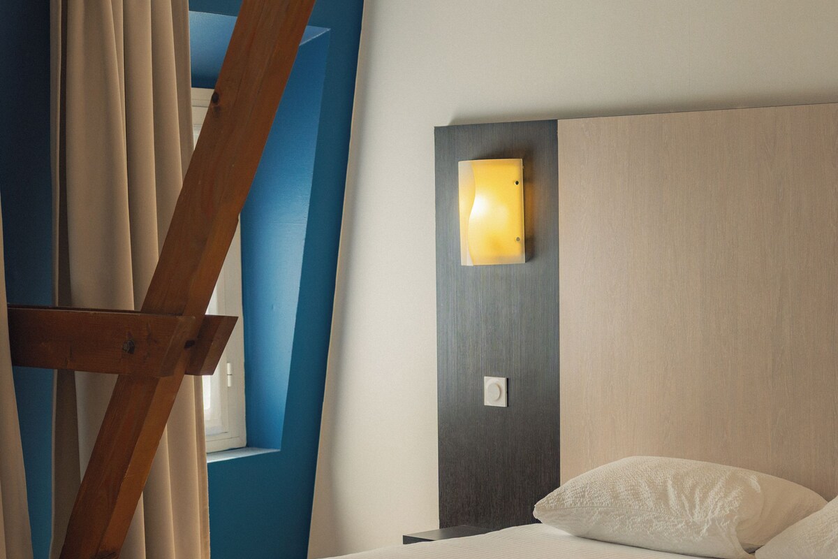 Une chambre à coucher moderne avec un lit, une table de chevet, une lampe fixée au mur et une fenêtre avec des rideaux.