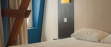 A modern bedroom with a bed, a nightstand, a wall-mounted lamp, and a window with curtains.