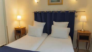 Uma cama de casal com duas almofadas brancas, uma cortina azul escura e duas luminárias de cabeceira.