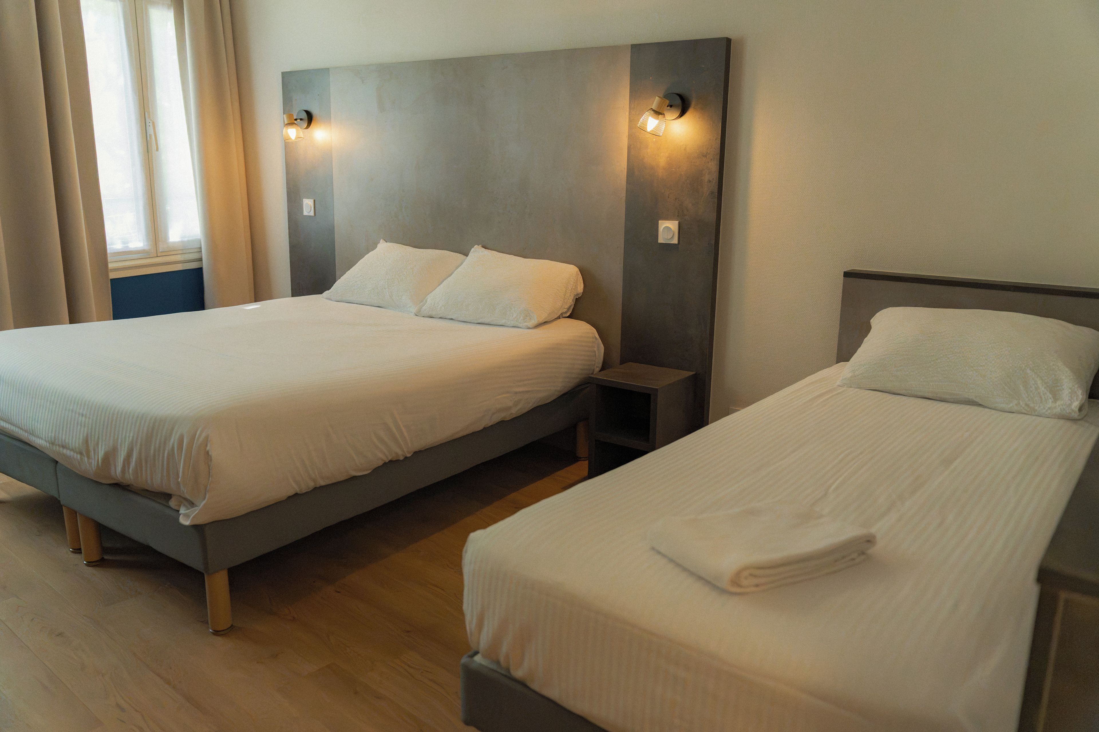 A hotel room with two single beds, each with a pillow and a small bedside table.