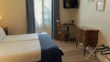Una habitación de hotel con cama, escritorio con silla, televisor y cómoda.