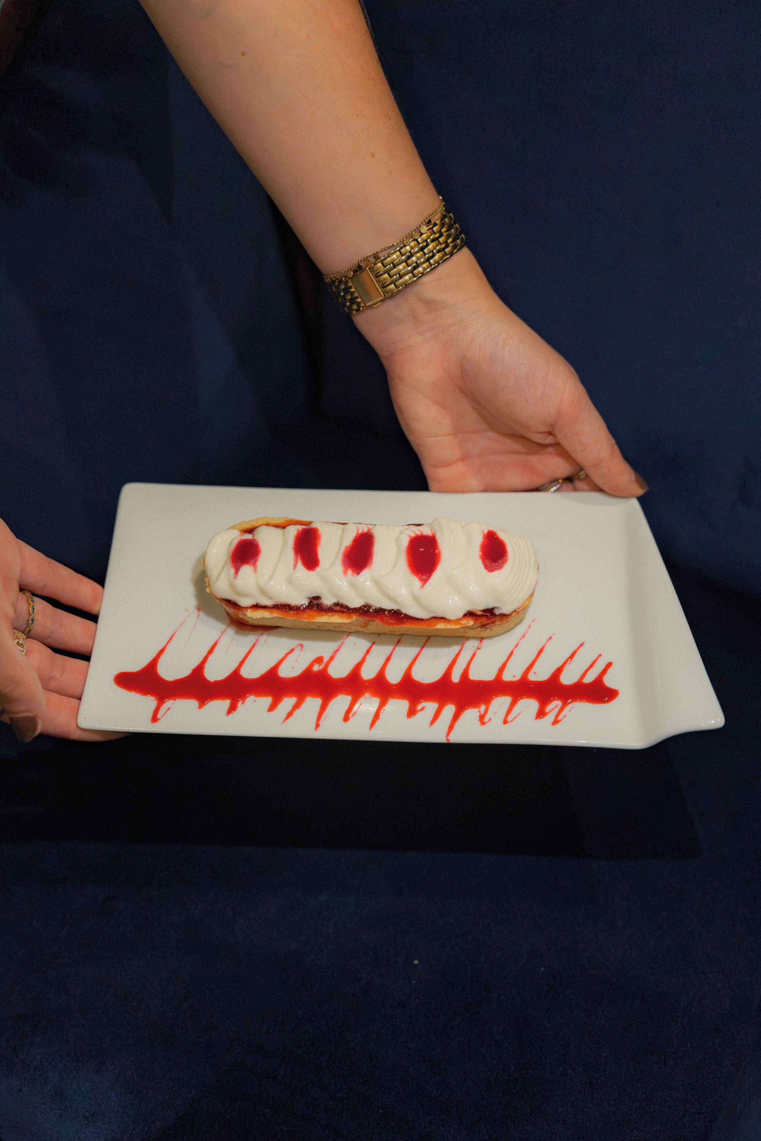 Una persona sosteniendo un postre con base blanca y cobertura roja, sobre un plato blanco con diseño rojo.