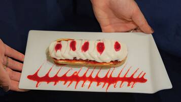 Una persona sosteniendo un postre con base blanca y cobertura roja, sobre un plato blanco con diseño rojo.