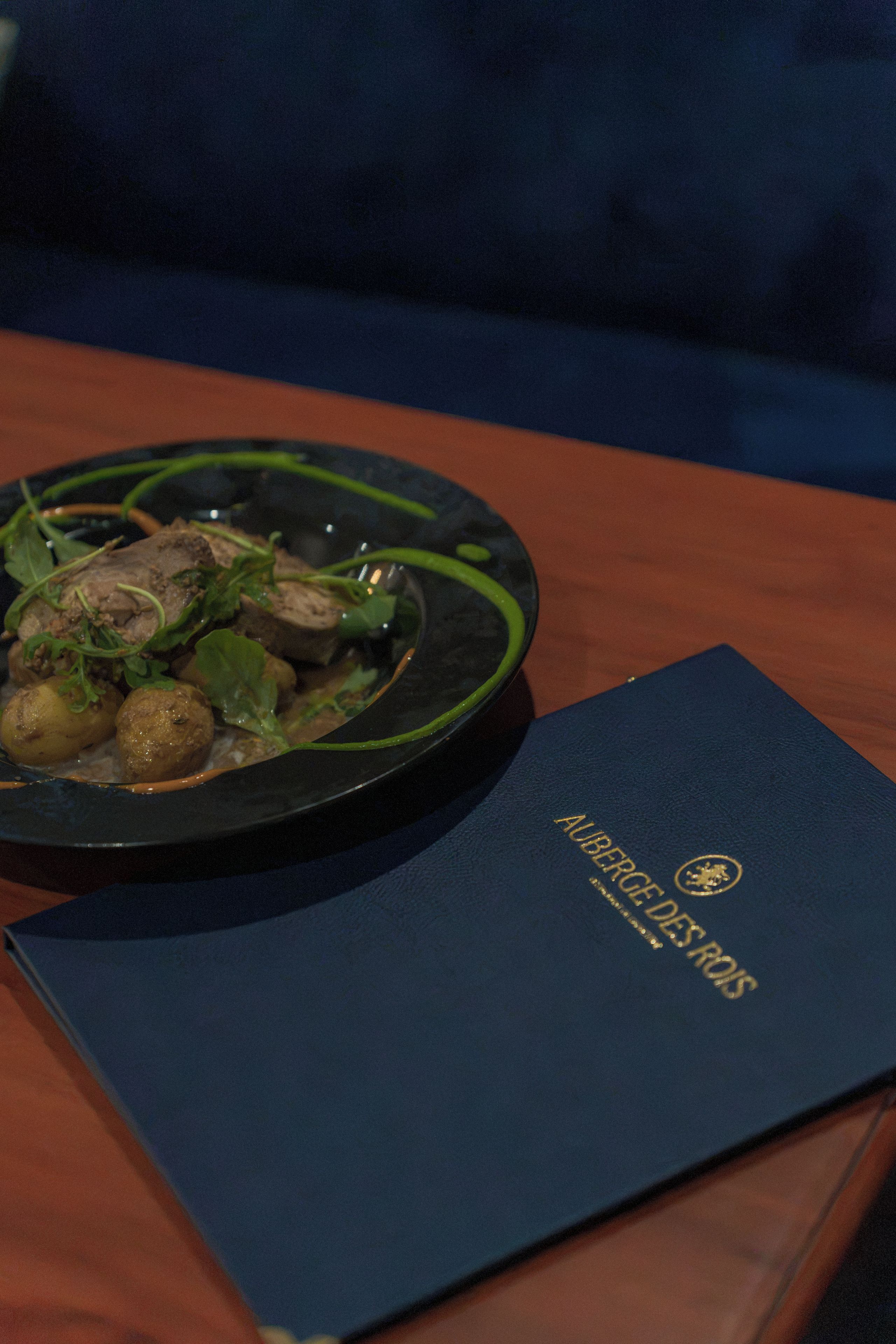 A plate of food with greens and meat, a blue booklet, and a dark blue couch.
