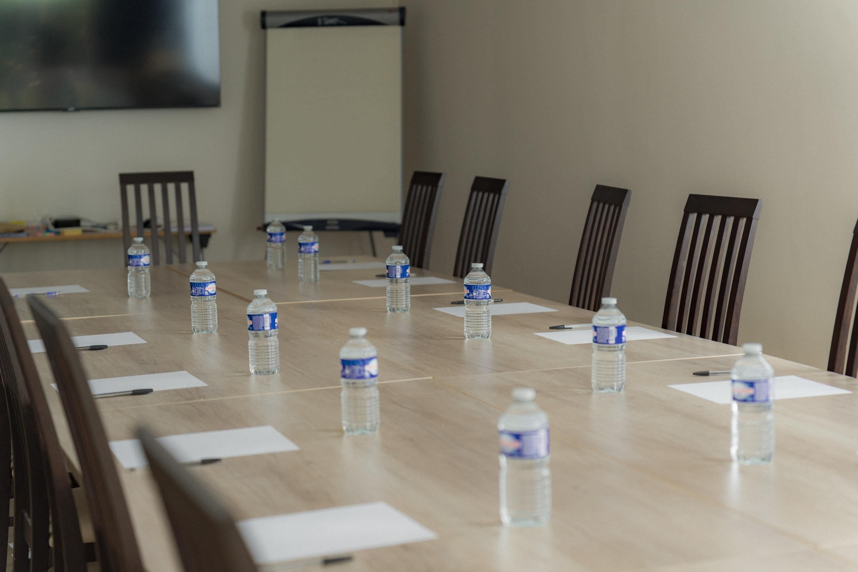 A conference room with a long table, chairs, water bottles, and a projector screen.