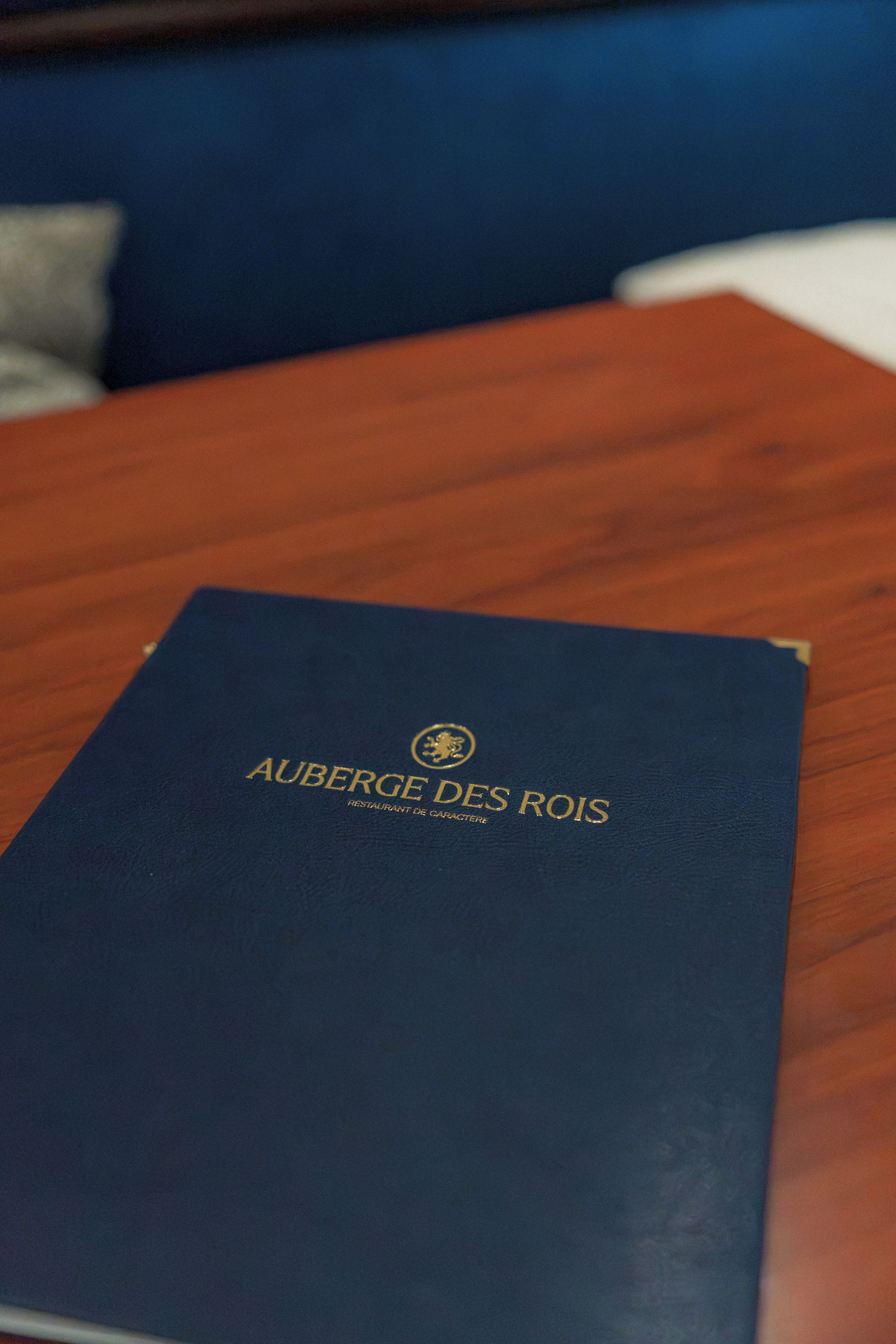 Un livre à la couverture bleu foncé intitulé « AUBERGE DES ROIS », posé sur une table en bois.