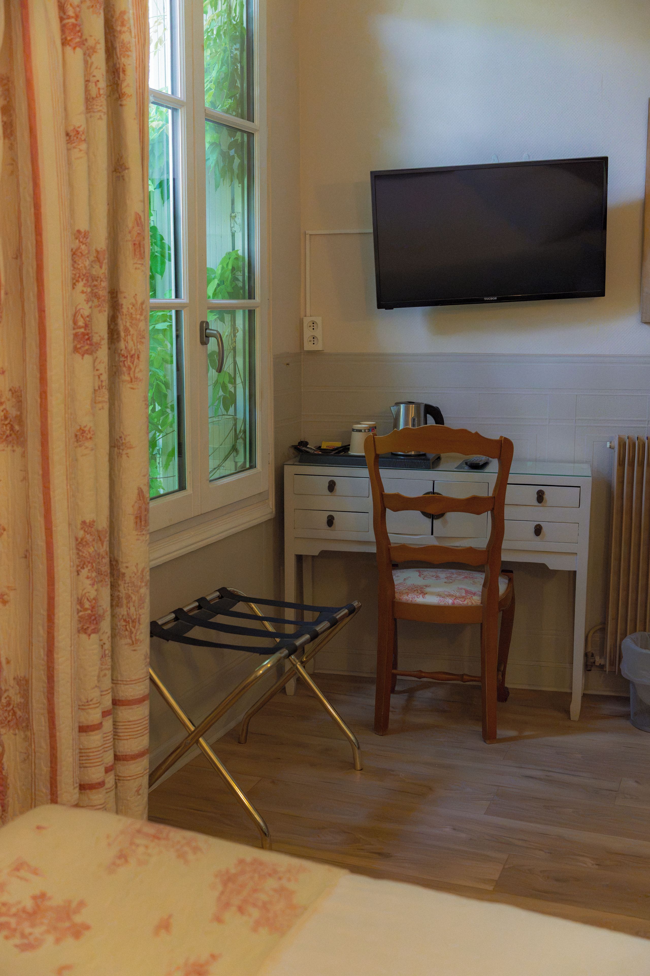 A room with a desk, a chair, a television mounted on the wall, and a window with curtains.