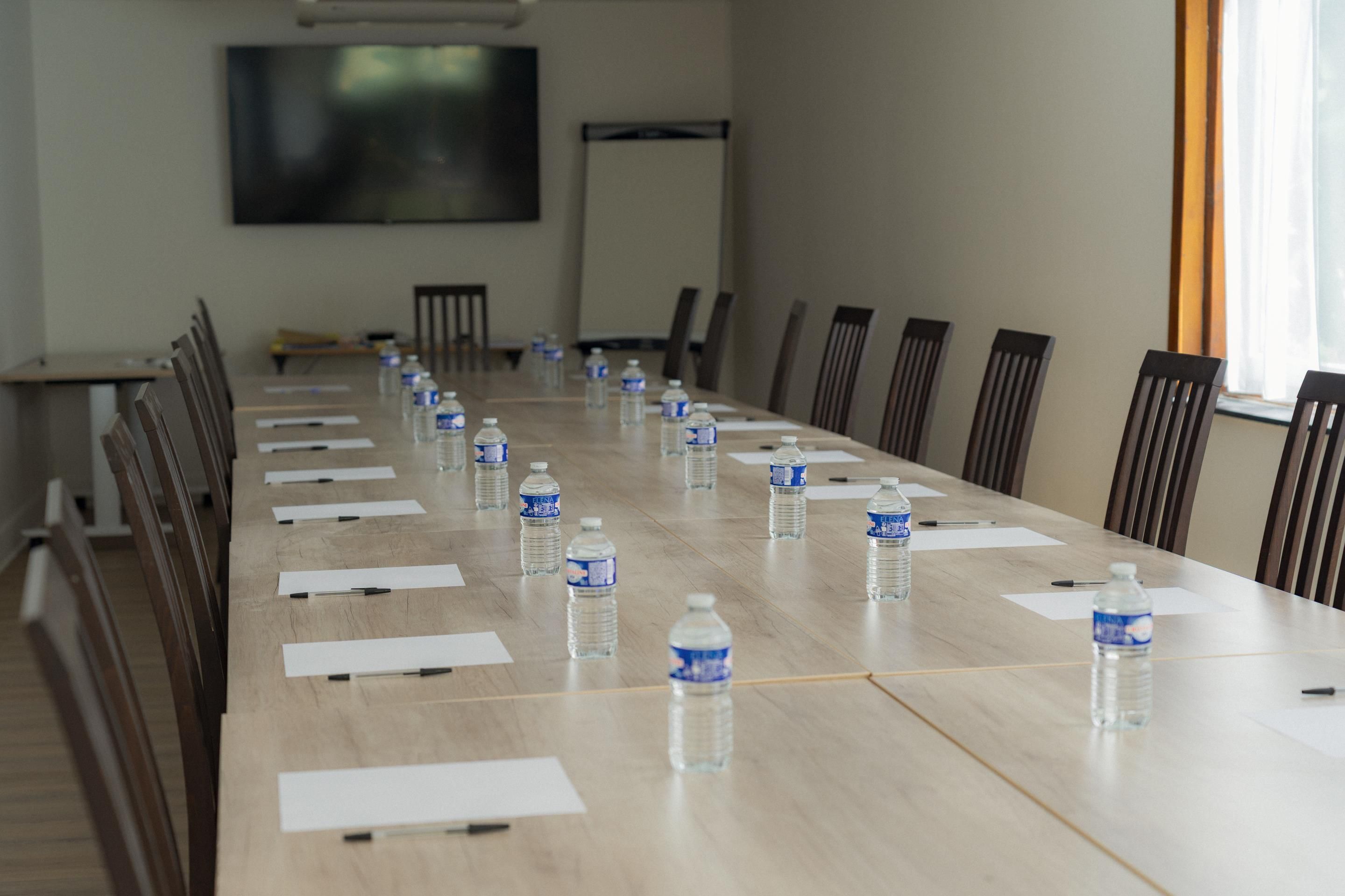 A conference room with a long table, chairs, water bottles, and papers.