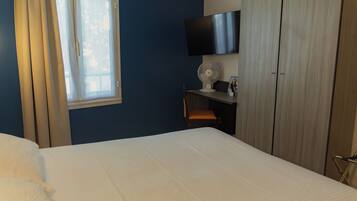 Quarto de hotel com cama, escrivaninha, cadeira, televisão e janela com cortinas.