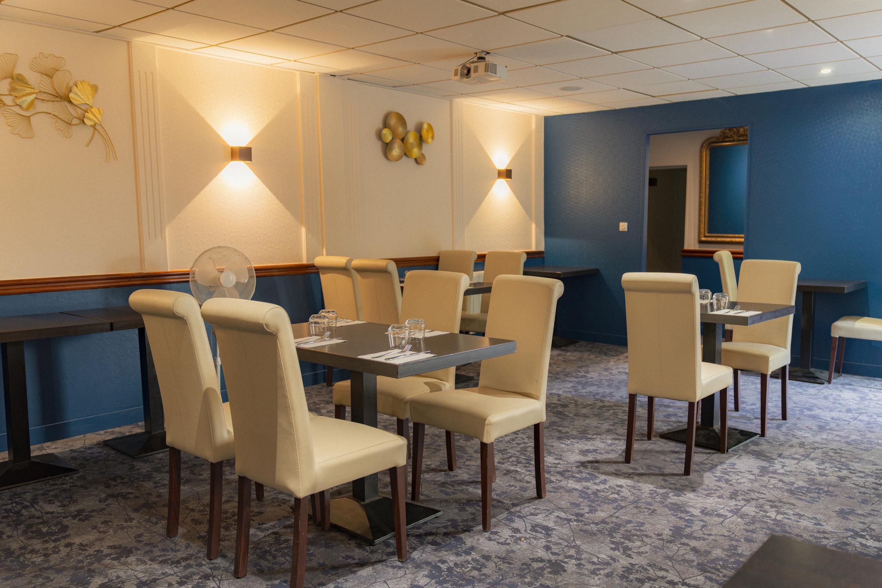 Un comedor de hotel con mesas y sillas, un proyector en el techo y decoración mural.