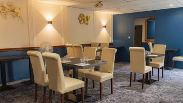 Un comedor de hotel con mesas y sillas, un proyector en el techo y decoración mural.