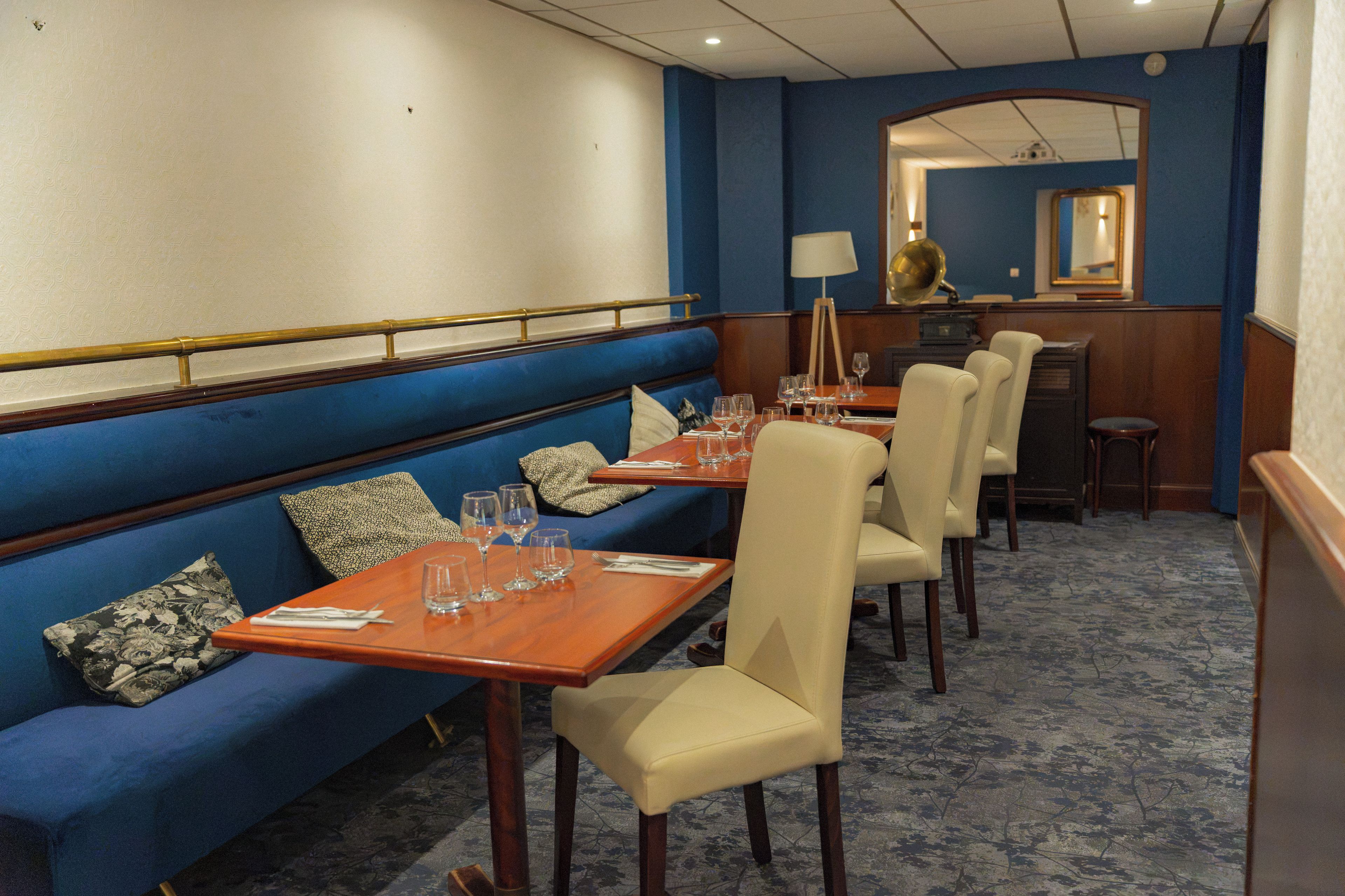 Een restaurantgedeelte in een hotel met een blauwe bank, houten tafels en roomwitte stoelen.