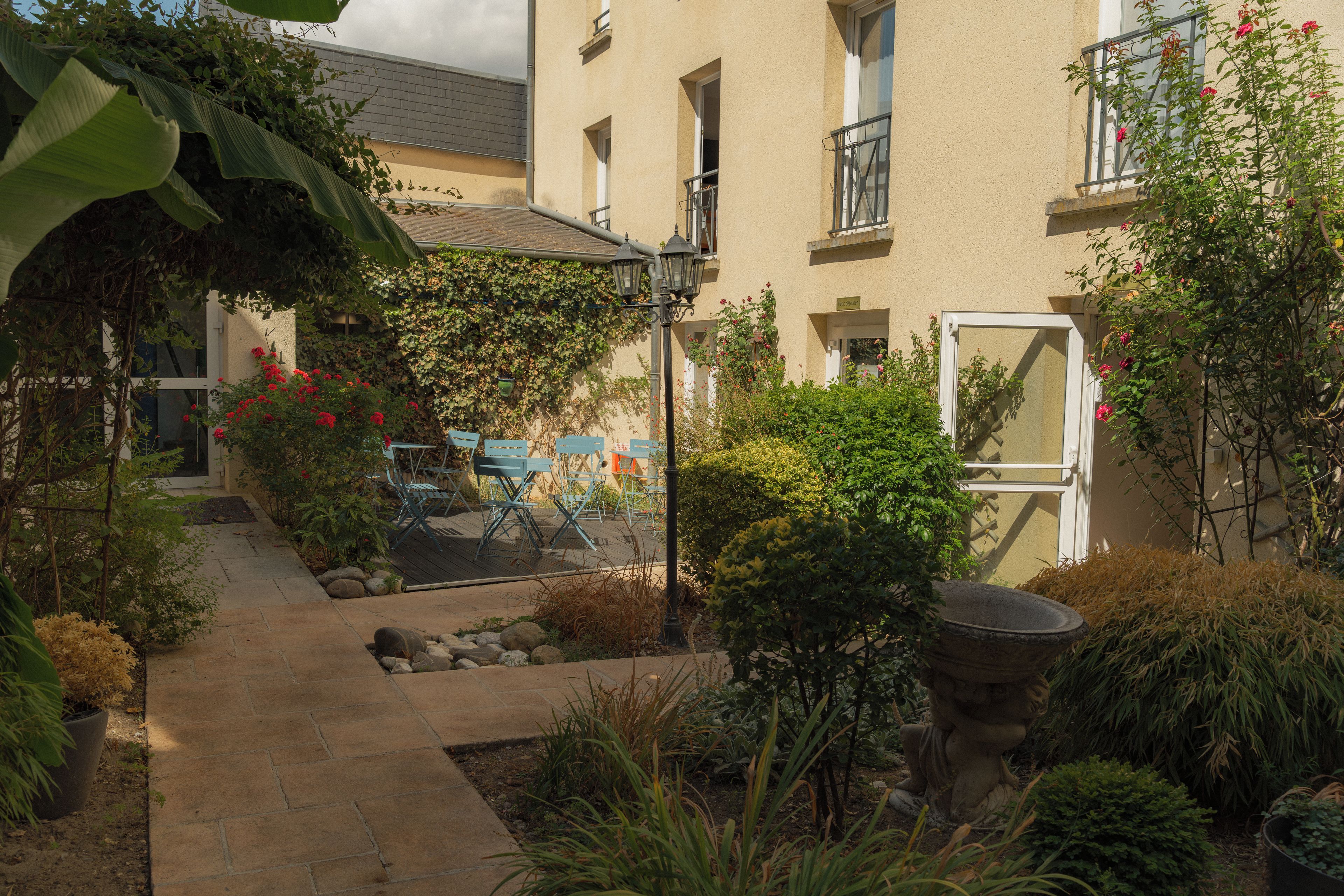 Une cour avec un chemin, un jardinière en pierre et un bâtiment doté d’un balcon.