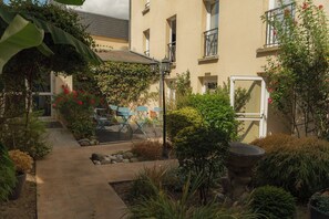 A courtyard with a pathway, a stone planter, and a building with a balcony. - Auberge des Rois - Chinon (Chinon)