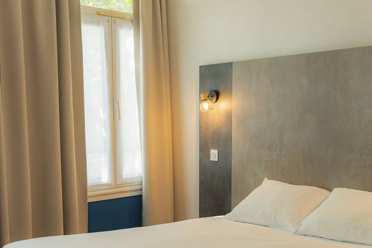 Une chambre à coucher avec un lit, des rideaux, une fenêtre et un luminaire fixé au mur.