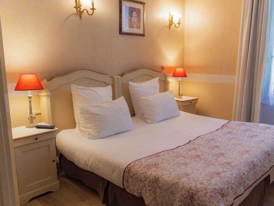 A hotel room with a bed, two bedside lamps, a nightstand, and a framed picture on the wall.