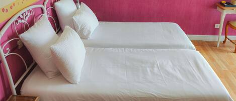 A double bed with white linens and pillows, a bedside table with a glass top, and a wooden chair.