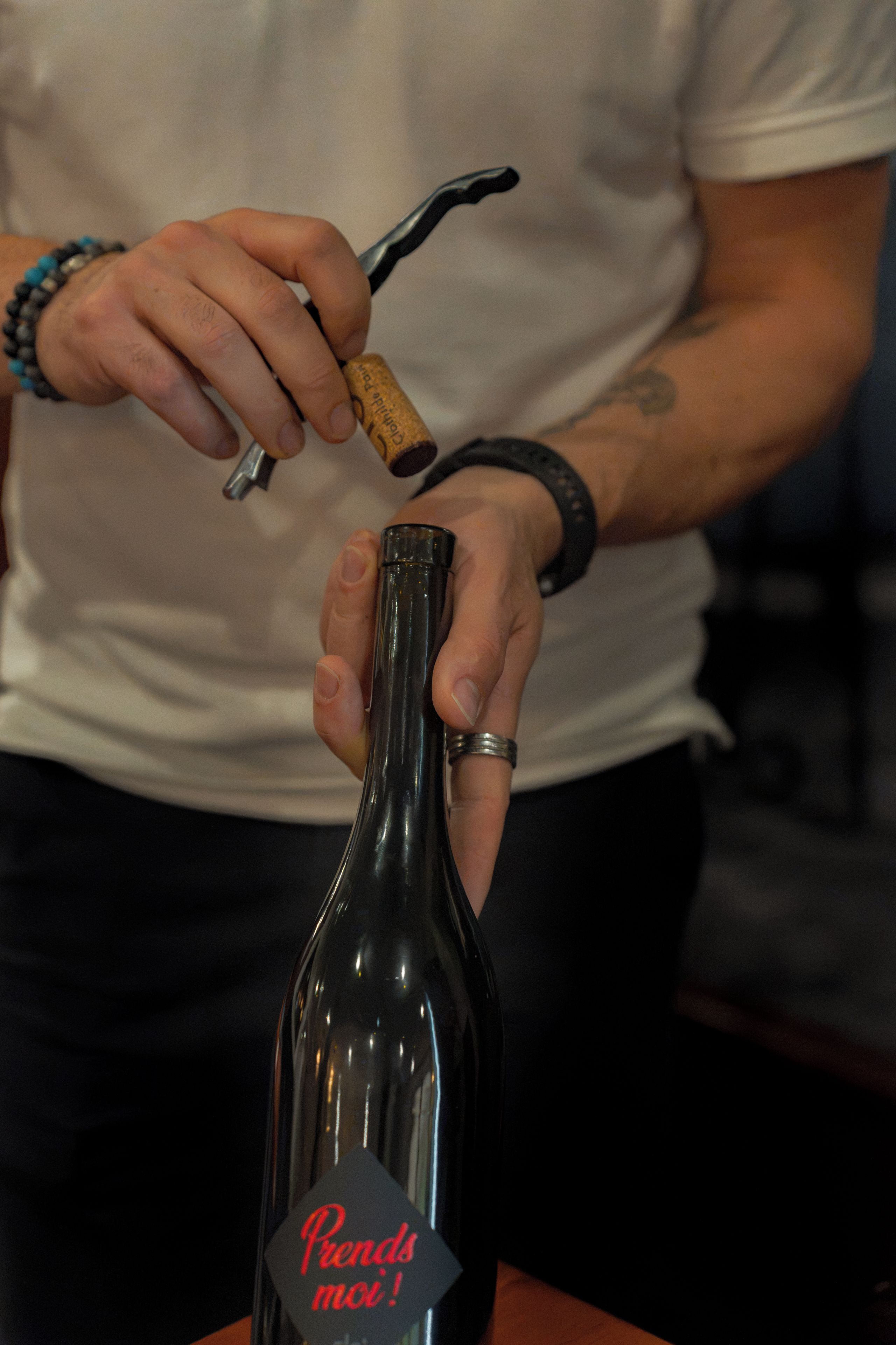 A person holding a corkscrew near a bottle with a tag that reads 'Prends moi!'