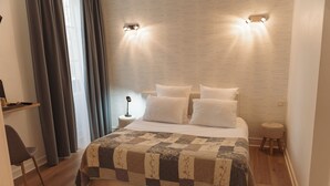 A bedroom with a large bed, a bedside table, a lamp, a chair, and a window with curtains. - Brit Hotel Chinon le Lion d'Or  (Chinon)