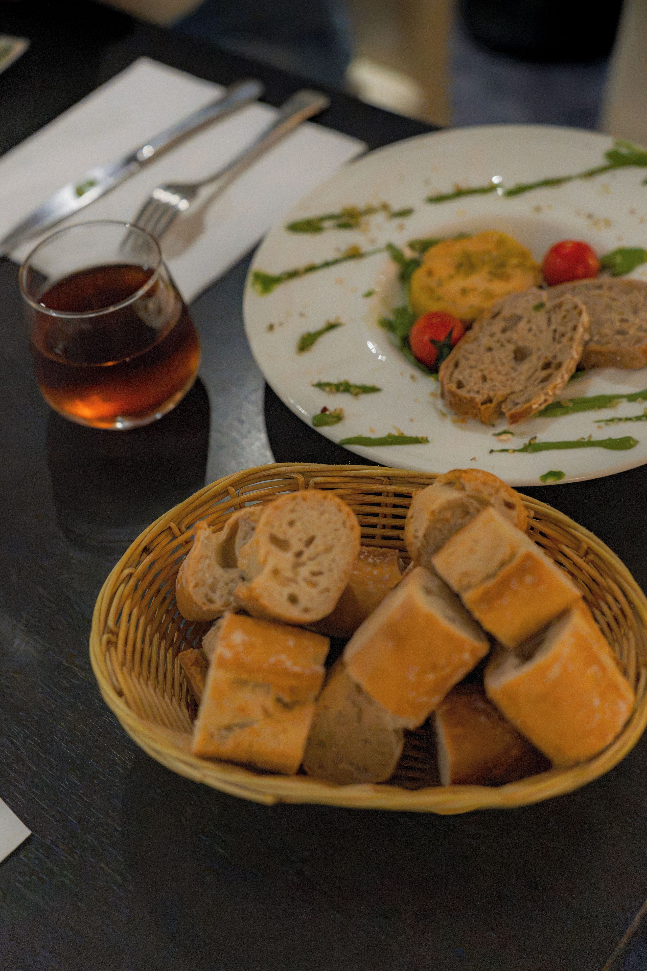 Une table à manger avec une assiette de nourriture, un panier de pain et un verre de thé.