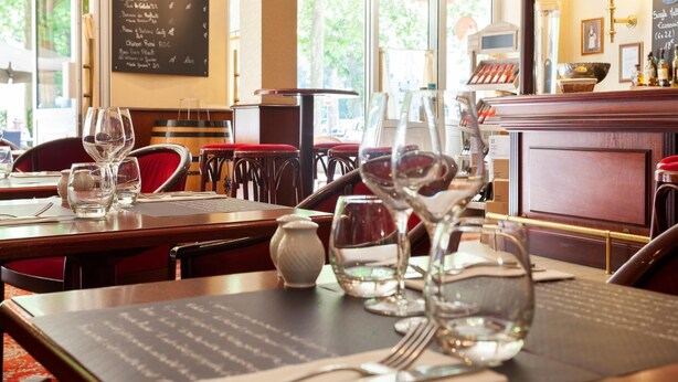 A restaurant interior with tables set for dining, menus on the wall, and a bar area visible in the background. - Brit Hotel Chinon le Lion d'Or  (Chinon)