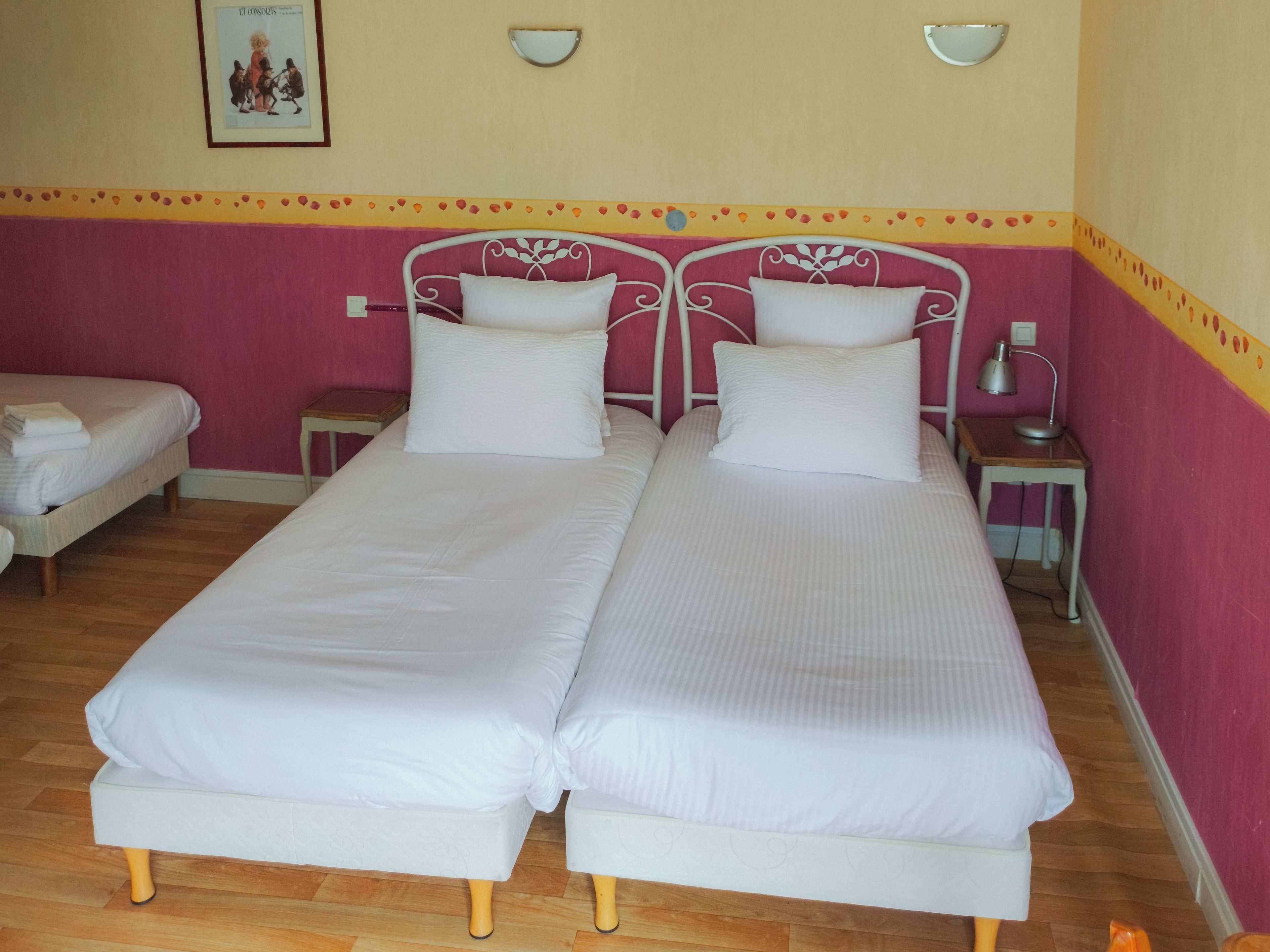 Una cama doble con ropa blanca en una habitación con paredes rosas y suelo de madera.