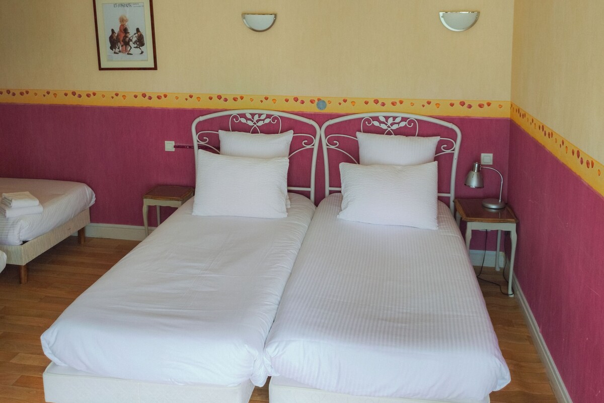 Un lit double avec une literie blanche, dans une chambre aux murs roses et au plancher en bois.