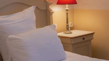 A bed with white linens and pillows, a bedside table with a red lamp, and a wall-mounted light fixture.