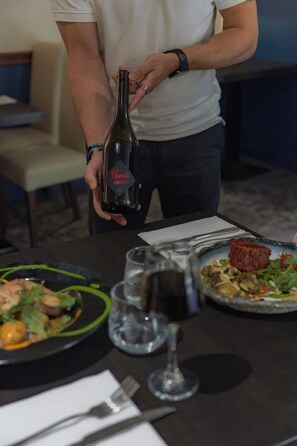 Une personne tenant une bouteille dont l’étiquette porte l’inscription « Prends-moi ! » et une assiette de nourriture posée sur une table.