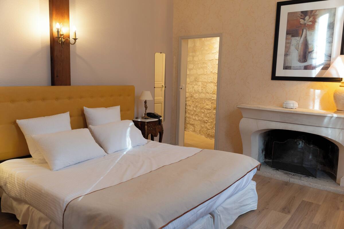 Une chambre à coucher avec un grand lit, une cheminée, une table de chevet et une lampe fixée au mur.