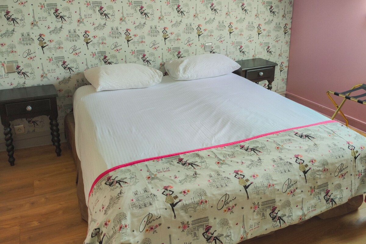 Un lit avec une housse de couette sur le thème de Paris, une table de chevet et une chaise.