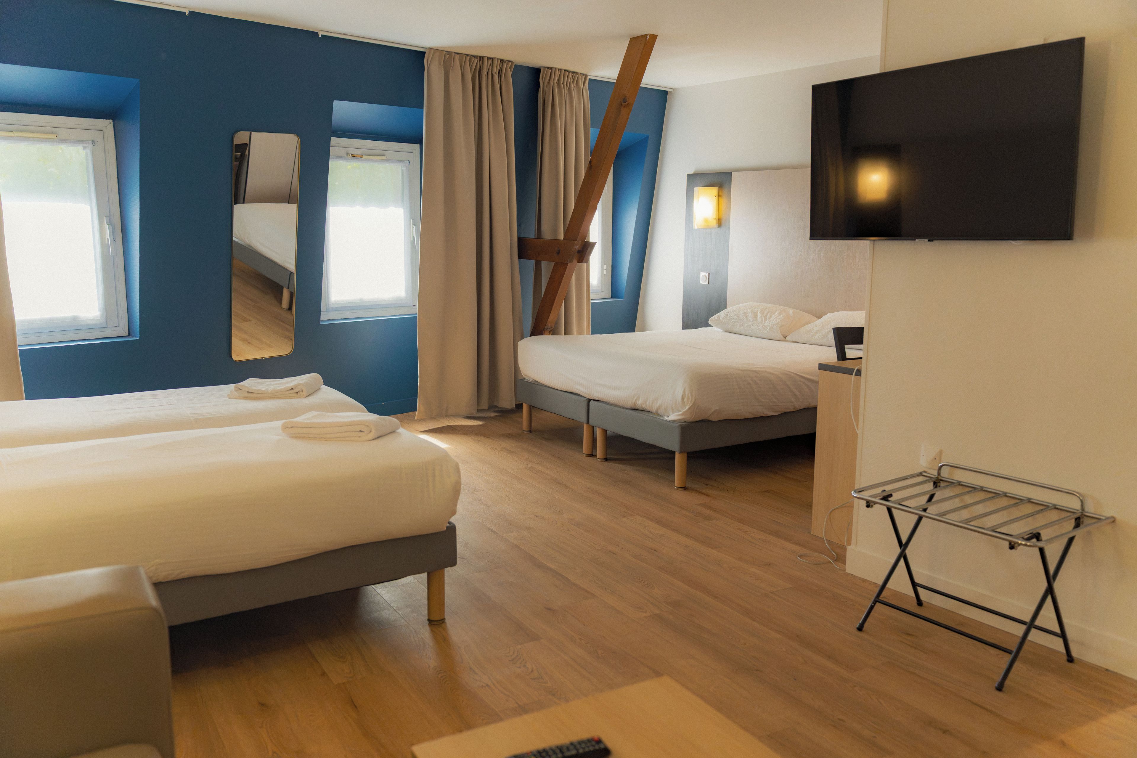 A hotel room with two beds, a TV, a mirror, and a window.