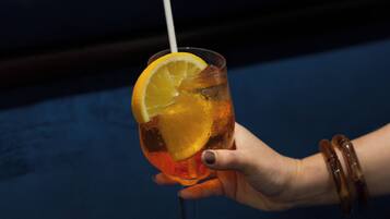 A hand holding a cocktail glass with a straw, containing a beverage and an orange slice garnish.