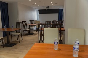 A hotel dining area with tables and chairs, water bottles on tables, and a projector screen on the wall.