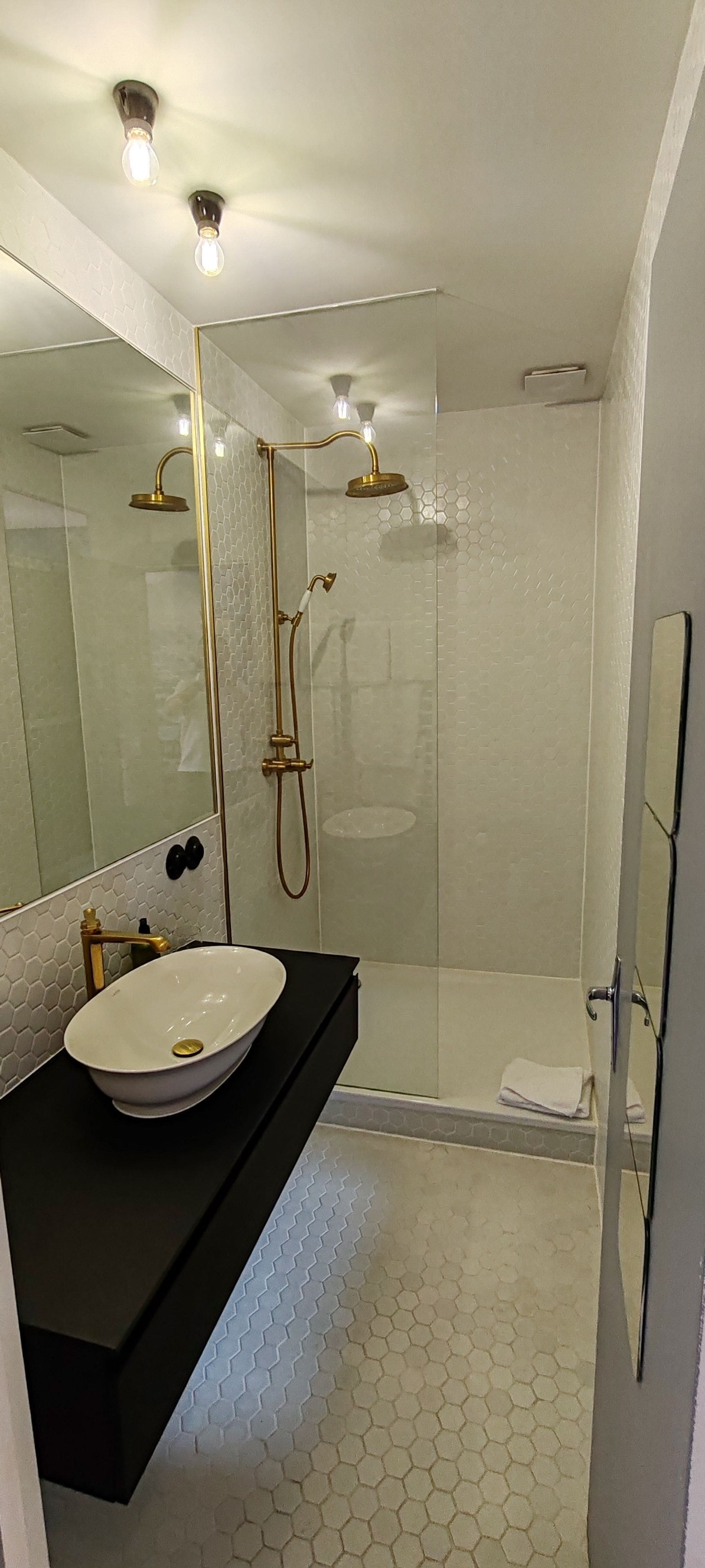 Ein modernes Badezimmer mit einem großen Spiegel, einem weißen Waschbecken, einer Dusche mit Glastür und einer schwarzen Arbeitsfläche.