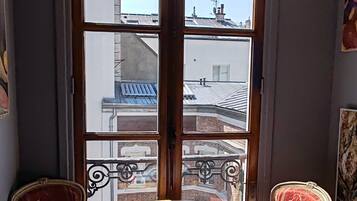 A room with a round table, two chairs, and a view of buildings through large windows.