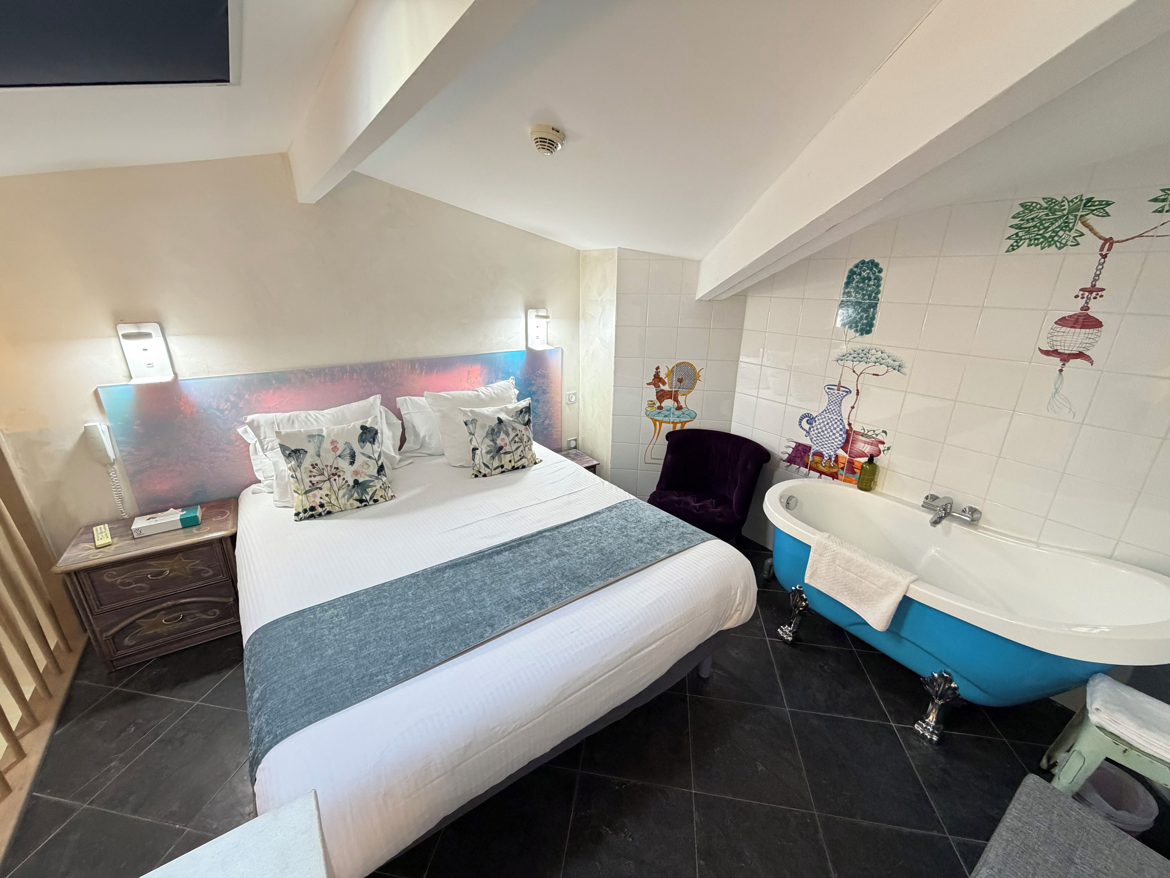 A hotel room with a bed, bedside table, phone, and a bathroom with a bathtub and shower.