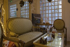 A vintage-style room with a patterned sofa, a small table with a vase and pinecones, and a painting on the wall. - Hotel le Pavillon (Paris)