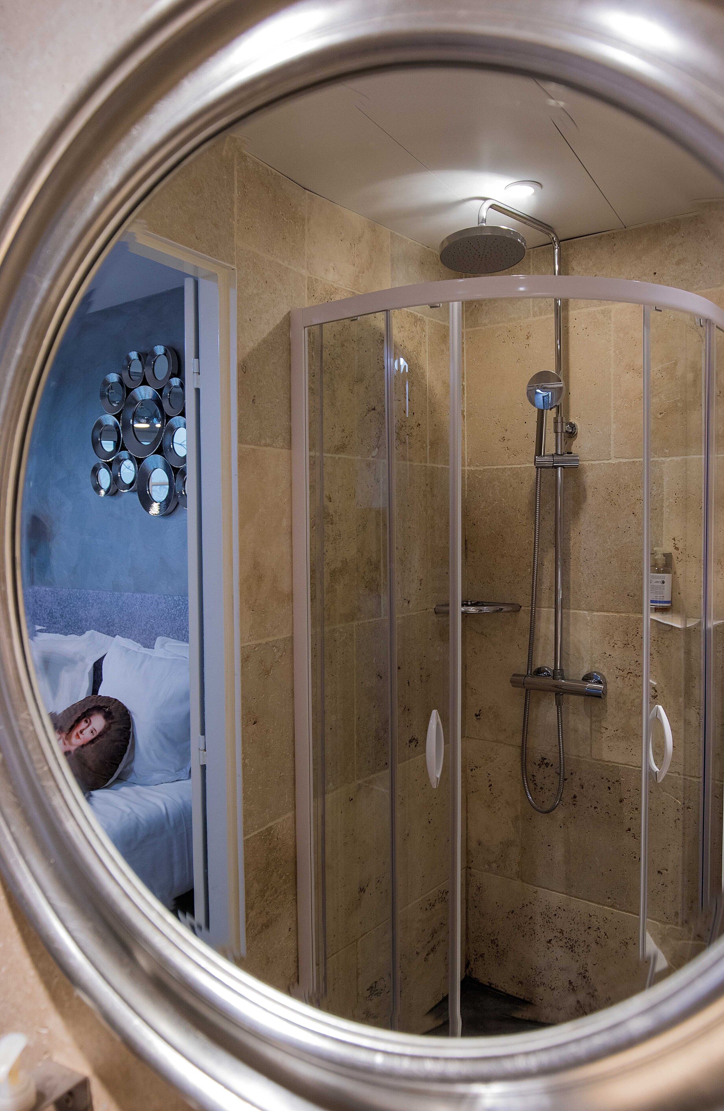 Une douche fermée par des parois en verre, dotée d’un pommeau de douche à main, d’un panneau de commande fixé au mur et d’un sol carrelé.